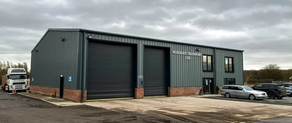 A steel-framed HGV workshop in Yorkshire, with several large bays for servicing and repairing heavy-duty vehicles, and a modern office space visible in the background.