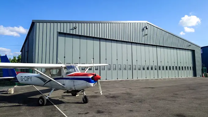 Large aircraft hangar in grey with concertina doors and a small aeroplane in the foreground at Elstree Aerodrome
